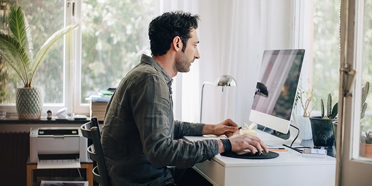 Side view of young businessman using computer while sitting at desk in home office